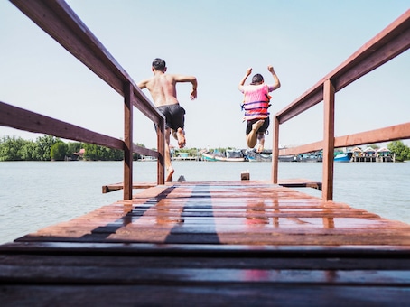 Man and his sister jumping off wooden bridge into river