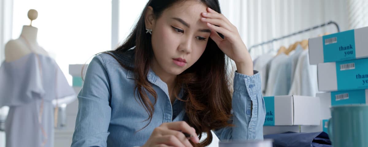 Young attractive asia female business owner thoughtful serious doubtful feel stress worry with financial problem in SME crisis small business challenges impact from covid coronavirus at home office.