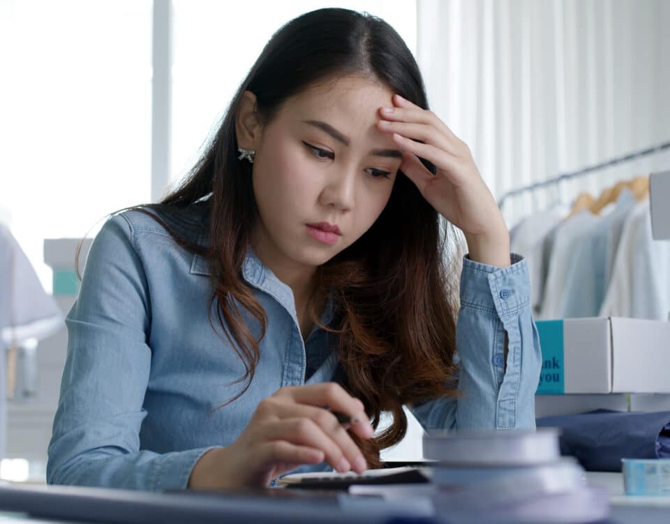 Young attractive asia female business owner thoughtful serious doubtful feel stress worry with financial problem in SME crisis small business challenges impact from covid coronavirus at home office.